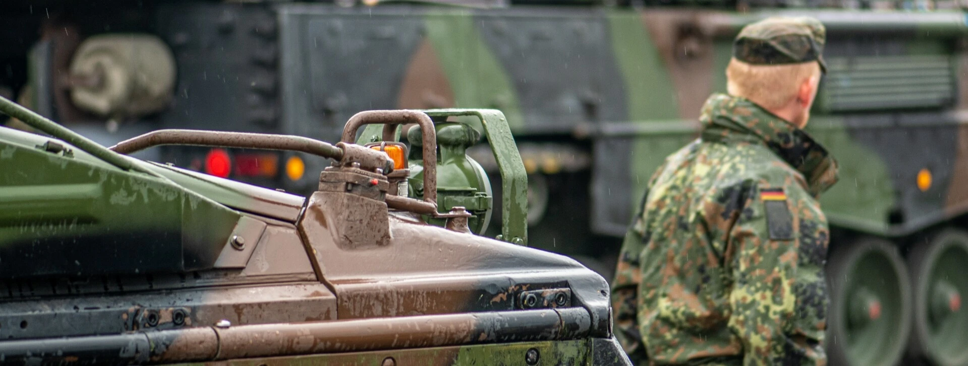Militärfahrzeug im Vordergrund und Soldat in Uniform, der sich von der Kamera abwendet.