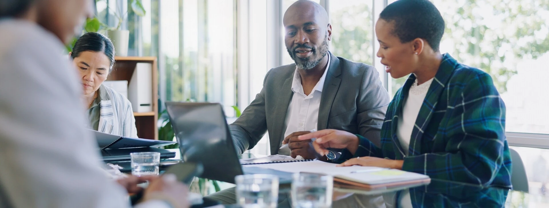 Diverse Geschäftsleute in einer Besprechung im Büro mit Laptops und Unterlagen auf dem Tisch.
