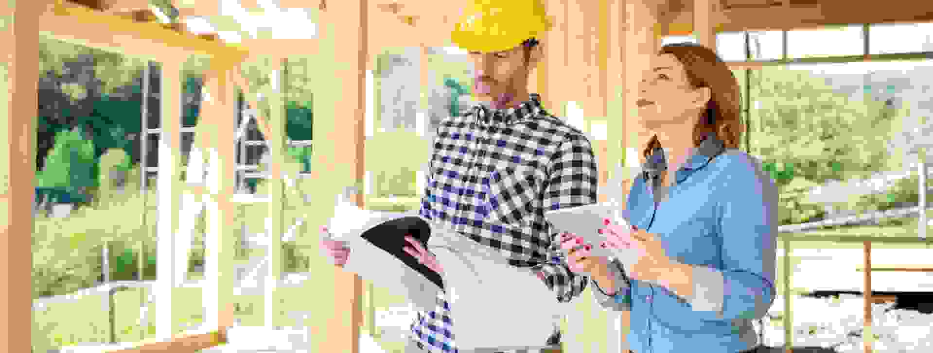 Ein Bauingenieur und eine Klientin besprechen Baupläne auf einer Holzhausbaustelle.