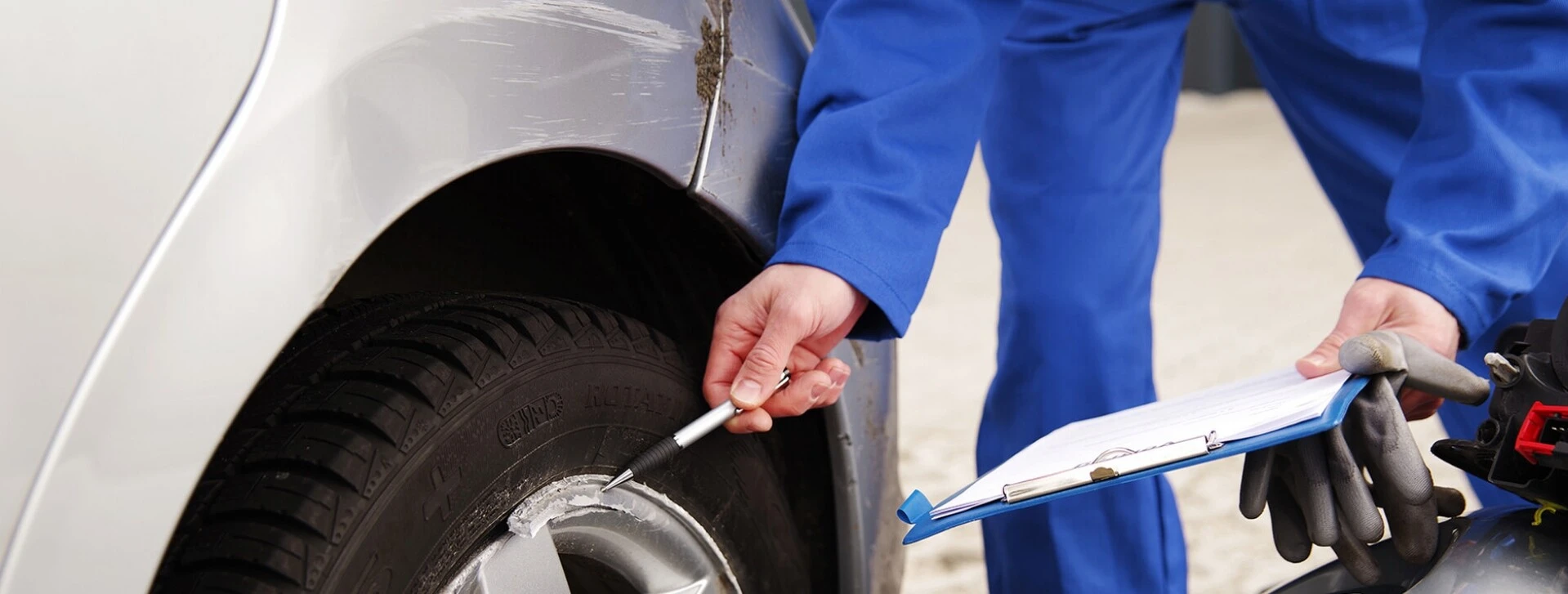 Mechaniker überprüft Schäden an einem Autoreifen mit einem Werkzeug und hält eine Klemmmappe.
