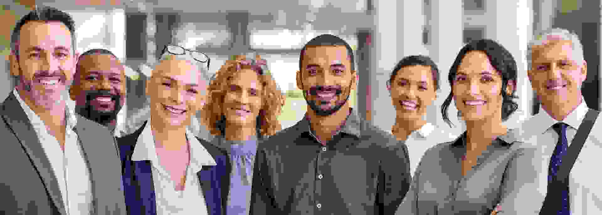 Gruppe diverser Dozenten und angehender Sachverständiger lächelnd in einem Bürogebäude stehend.