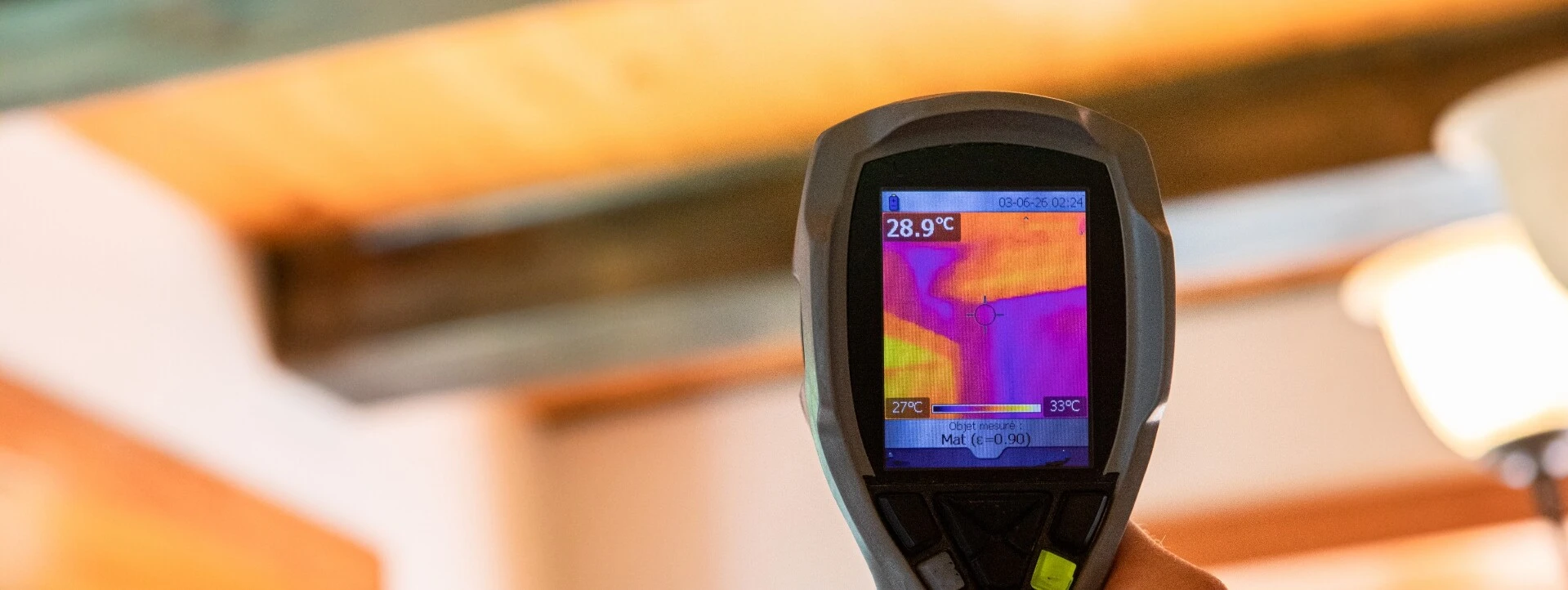 Hand hält ein Wärmebildkamera-Gerät, das die Temperaturverteilung an einer Decke anzeigt.