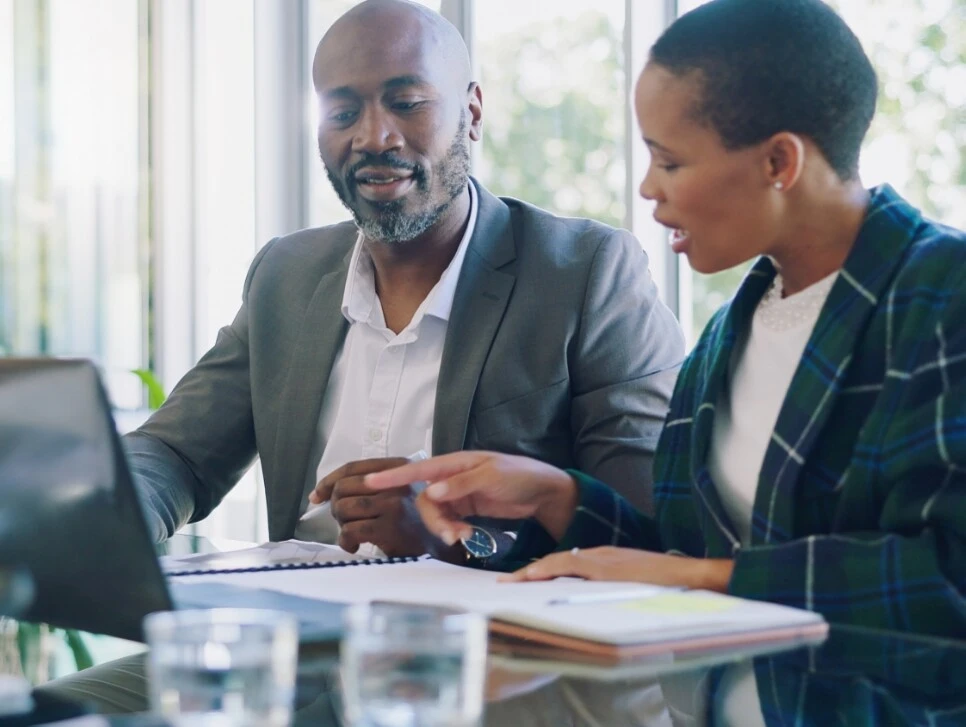 Diverse Geschäftsleute in einer Besprechung im Büro mit Laptops und Unterlagen auf dem Tisch.