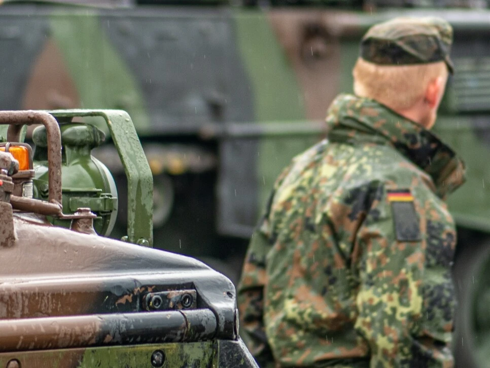 Militärfahrzeug im Vordergrund und Soldat in Uniform, der sich von der Kamera abwendet.