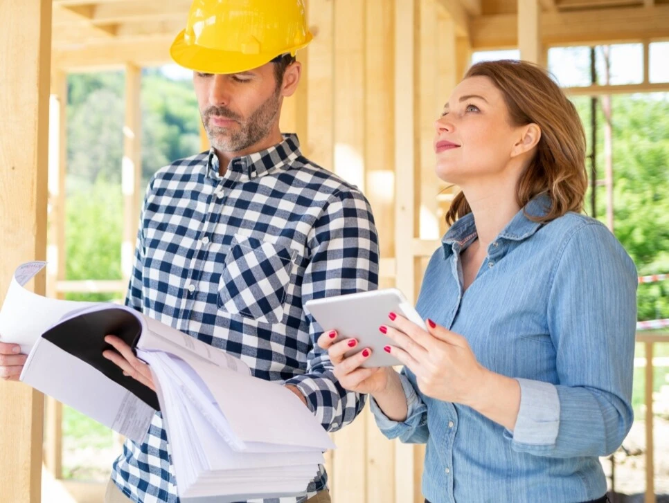 Ein Bauingenieur und eine Klientin besprechen Baupläne auf einer Holzhausbaustelle.
