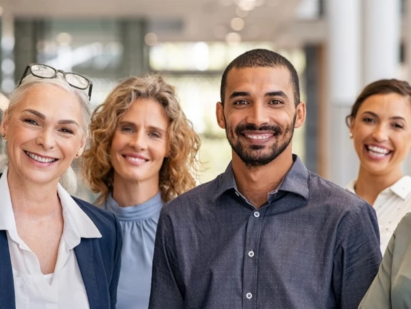Gruppe diverser Dozenten und angehender Sachverständiger lächelnd in einem Bürogebäude stehend.