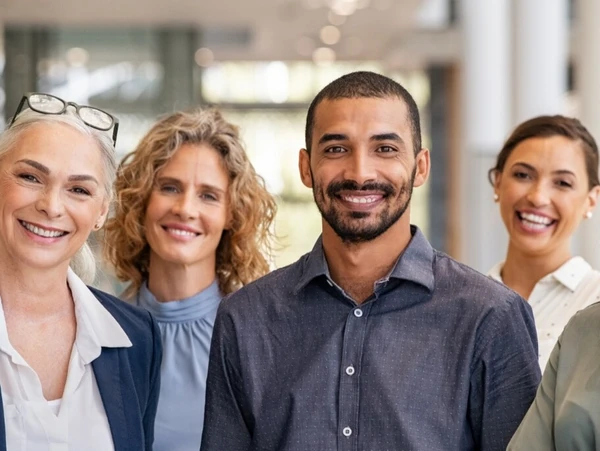 Gruppe diverser Dozenten und angehender Sachverständiger lächelnd in einem Bürogebäude stehend.