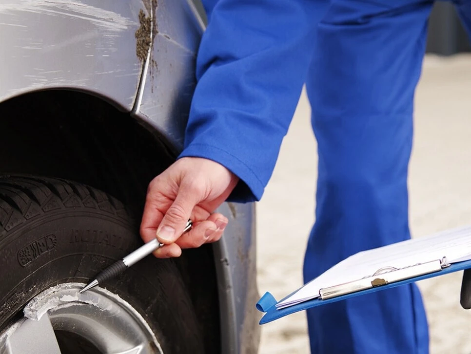 Mechaniker überprüft Schäden an einem Autoreifen mit einem Werkzeug und hält eine Klemmmappe.