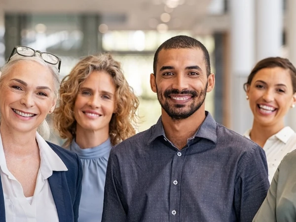 Gruppe diverser Dozenten und angehender Sachverständiger lächelnd in einem Bürogebäude stehend.