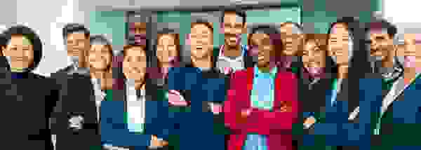 Gruppenfoto von lächelnden Mitarbeitern verschiedener Ethnien in formeller Kleidung.