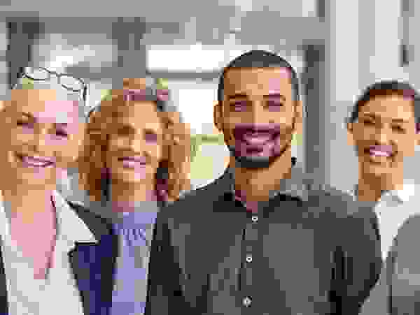 Gruppe diverser Dozenten und angehender Sachverständiger lächelnd in einem Bürogebäude stehend.